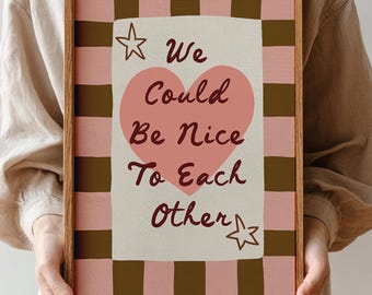 Può includere: Una stampa artistica incorniciata con il messaggio "We Could Be Nice To Each Other". L'opera presenta un cuore rosa, stelle e uno sfondo a scacchi rosa e marrone. La cornice è in legno.