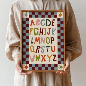 Peut inclure: Une affiche encadrée de l'alphabet, avec les lettres A à Z de couleurs vives. Les lettres sont sur un fond crème. Le cadre présente un motif de damier rouge, bleu et crème, avec des étoiles décoratives.
