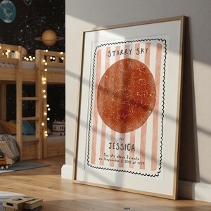 May include: A framed print featuring a watercolor illustration of a starry sky. The design includes a large, reddish-orange circle with constellations, set against a background of pink and white stripes. Text reads "Starry Sky" and "for Jessica".
