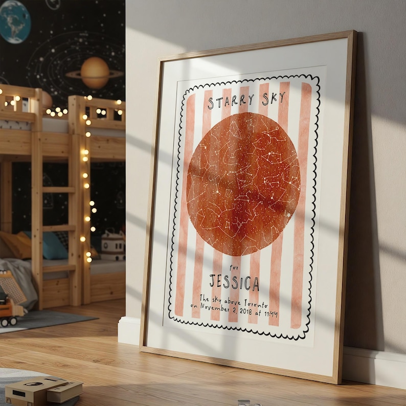 May include: A framed print featuring a watercolor illustration of a starry sky. The design includes a large, reddish-orange circle with constellations, set against a background of pink and white stripes. Text reads "Starry Sky" and "for Jessica".