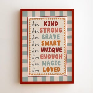 Op de afbeelding: Een rechthoekige wandprint in een rode lijst met een lichtblauwe en witte gestreepte rand. Het midden bevat de tekst: I am KIND, I am STRONG, I am BRAVE, I am SMART, I am UNIQUE, I am ENOUGH, I am MAGIC, I am LOVED in verschillende kleuren.
