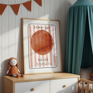 May include: A framed print with a star map design. The print features a large, reddish-orange circle with white star constellations, set against a background of pink and white stripes. Text reads "STARRY SKY" and "for JESSICA".
