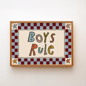 May include: A framed art print with the words "BOYS RULE" in colourful, playful lettering. The artwork features a cream-coloured background with a dotted border, surrounded by a red and blue chequered pattern and star accents.