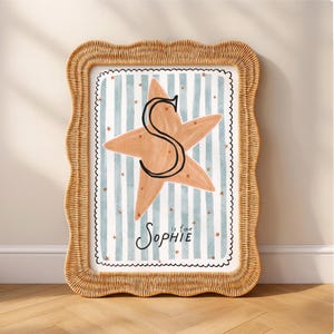 Pode incluir: Uma impressão emoldurada com uma borda tecida marrom claro. A obra de arte apresenta uma grande estrela do mar laranja com um "S" preto em um fundo listrado azul e branco. O texto "S is for Sophie" está escrito em itálico.