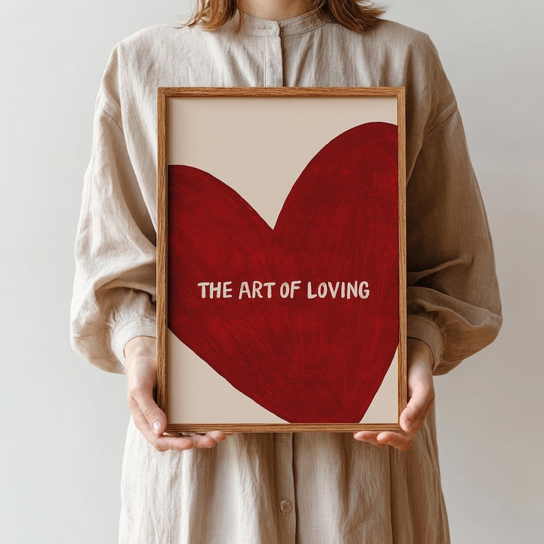 May include: A framed art print featuring a large red heart on a cream background. The text "THE ART OF LOVING" is displayed in white at the bottom of the heart. The frame is a light brown color.