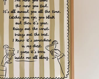 May include: A framed print with a light brown and white striped background. The print features black text with a poem about finding something within. Two hands are illustrated holding cocktail glasses. The frame is light brown.