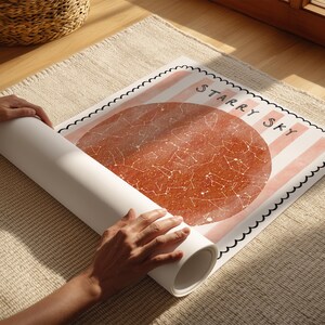May include: A rolled-up poster with a celestial map design is being unrolled. The poster features a large, reddish-brown circle with constellations and the words "Starry Sky" in black. The background has pink stripes.