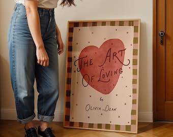 May include: A framed art print titled "The Art of Loving" by Olivia Dean. The artwork features a large red heart with the title in elegant script. The print has a pink background with red stars and a checkered border.