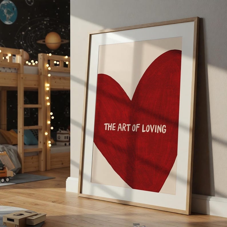 May include: Framed art print featuring a large red heart shape against a cream background. The text "THE ART OF LOVING" is centered within the heart. The artwork is displayed in a light wood frame.