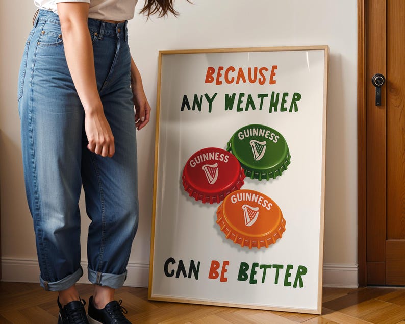 May include: A framed poster with the text "BECAUSE ANY WEATHER CAN BE BETTER." The poster features three Guinness bottle caps in red, green, and orange, each with a white harp symbol. The poster is displayed against a white background.