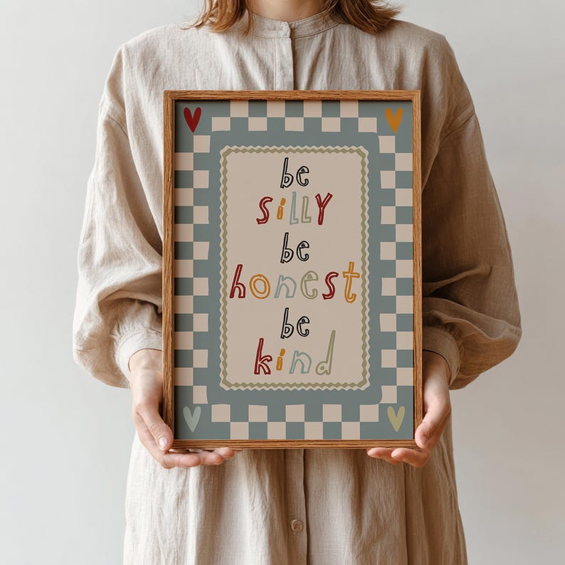 Pode incluir: Uma impress&atilde;o art&iacute;stica emoldurada com as palavras "be silly, be honest, be kind" em letras coloridas. A impress&atilde;o tem uma borda xadrez azul claro e branco. Uma pessoa segura a impress&atilde;o.