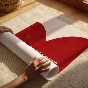 May include: A rolled-up white poster with a large red heart design. The poster is being unrolled on a beige rug. The text "Just Keep Loving" is visible on the poster.