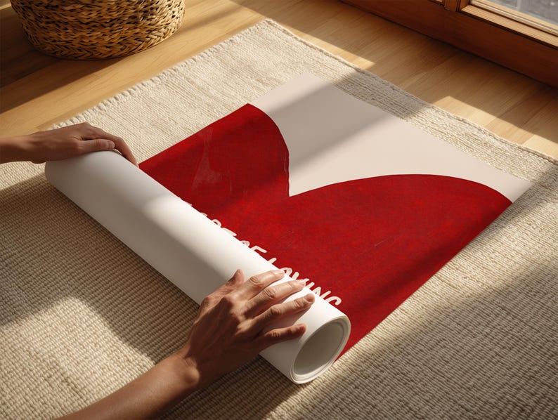 May include: A rolled-up white poster with a large red heart design. The poster is being unrolled on a beige rug. The text "Just Keep Loving" is visible on the poster.