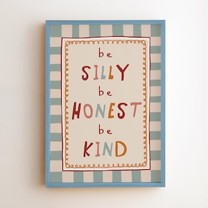 May include: A framed wall art print featuring a beige background with a blue and white striped border. The text reads "be SILLY be HONEST be KIND" in multi-colored, hand-drawn style lettering. A decorative orange scalloped line frames the text.