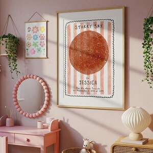 May include: A framed print with the text "STARRY SKY" and "for JESSICA". The print features a reddish-brown circle with constellations, set against a pink and white striped background. The room also includes a pink vanity, mirror, and floral art.