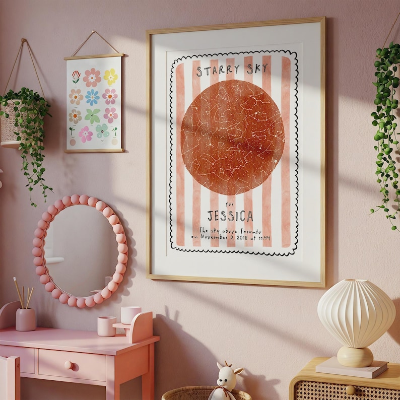 May include: A framed print with the text "STARRY SKY" and "for JESSICA". The print features a reddish-brown circle with constellations, set against a pink and white striped background. The room also includes a pink vanity, mirror, and floral art.