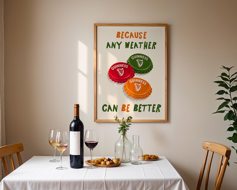 May include: A framed print with the text "BECAUSE ANY WEATHER CAN BE BETTER" and three Guinness bottle caps in red, green, and orange. A bottle of wine, wine glasses, and snacks are on a white tablecloth.