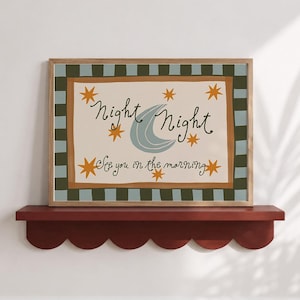 May include: A rectangular framed wall art print featuring a light blue crescent moon and orange stars on a cream background. The text reads Night Night and See you in the morning. The border has a dark green and light blue checkered pattern.
