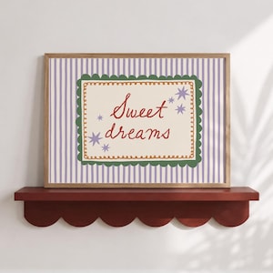 May include: A rectangular framed print featuring a light purple and white vertical striped background. The center displays a cream-colored rectangle with a scalloped green border, orange decorative trim, and the red text Sweet dreams with purple stars.