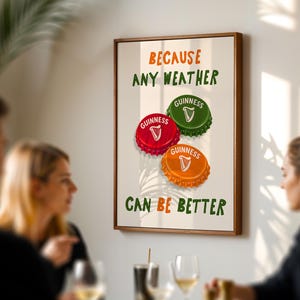 May include: A framed print featuring three Guinness bottle caps in red, green, and orange. The text reads "BECAUSE ANY WEATHER CAN BE BETTER" in green and orange. The print is displayed on a wall.