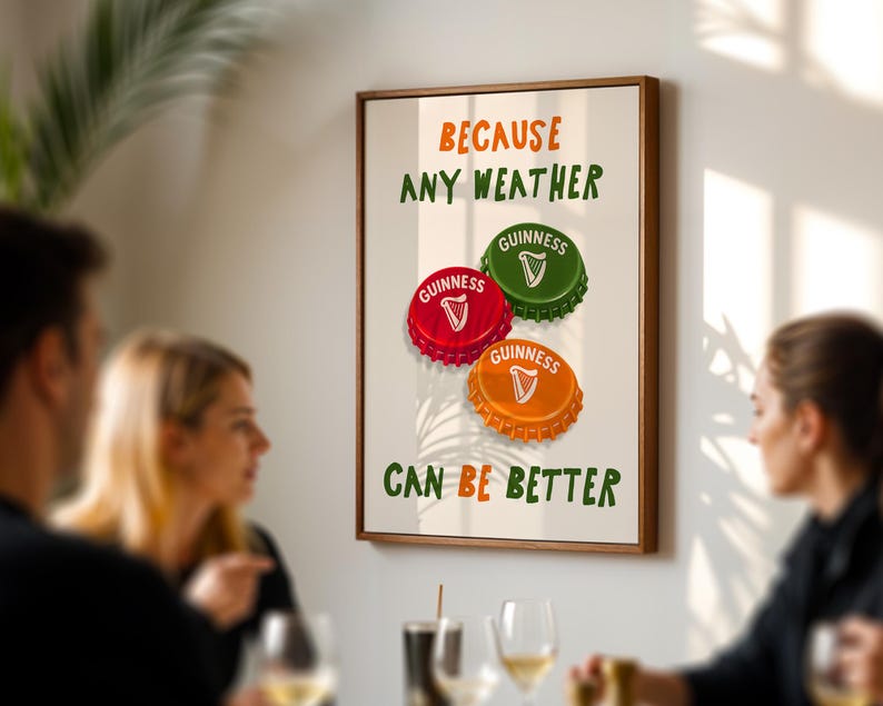 May include: A framed print featuring three Guinness bottle caps in red, green, and orange. The text reads "BECAUSE ANY WEATHER CAN BE BETTER" in green and orange. The print is displayed on a wall.