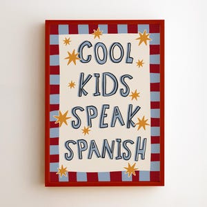 Peut inclure: Une affiche encadrée rectangulaire avec un fond crème et le texte bleu COOL KIDS SPEAK SPANISH. Le design comprend des illustrations d'étoiles jaunes et une bordure composée de rayures verticales alternées en rouge et bleu clair.
