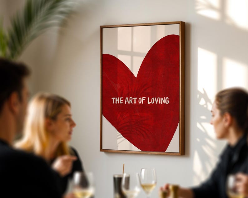 May include: A framed art print featuring a large red heart with the words "THE ART OF LOVING" in white. The artwork is displayed on a white background and framed in a wooden frame. The image is hanging on a wall.