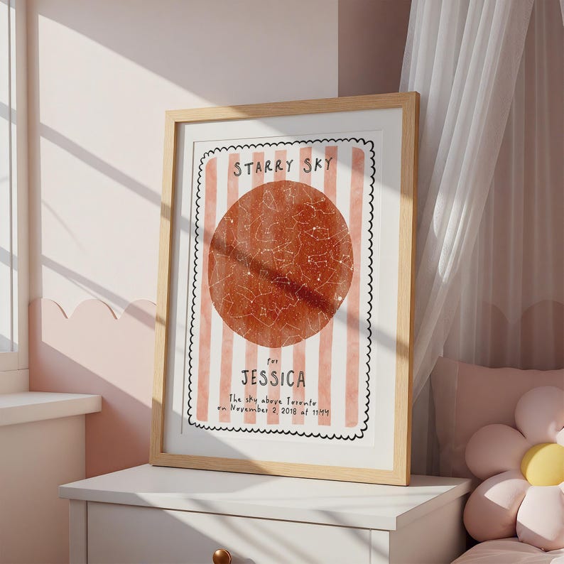 May include: Framed print with a light wood frame. The print features a red circle with a star map design, set against a background of pink and white stripes. Text reads "Starry Sky" and "for Jessica".