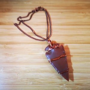 May include: A copper chain necklace with a brown arrowhead pendant wrapped in copper wire.