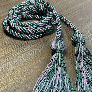 May include: Two green and pink tassel cords with a twisted rope design. The cords are tied together and the tassels are hanging down.