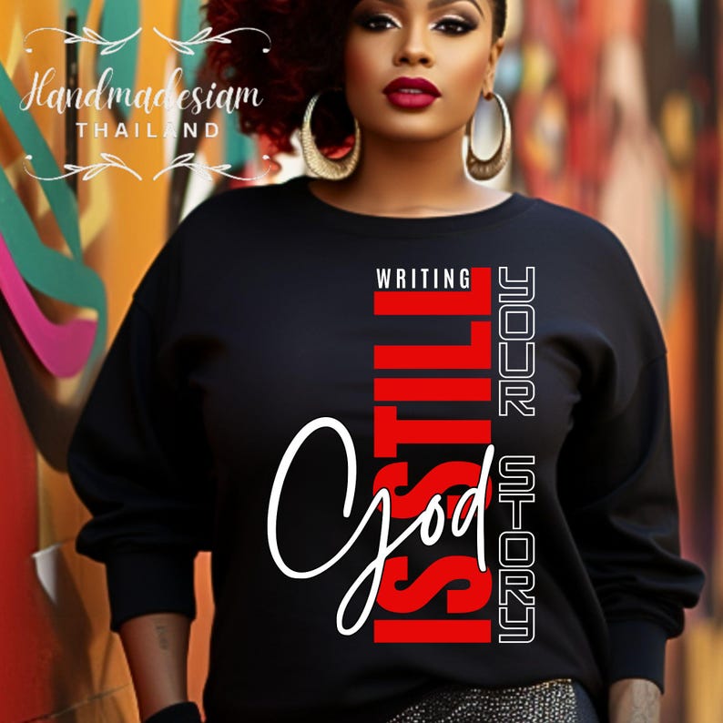 May include: Black sweatshirt with a white cursive "God" and red vertical text that reads "Is Still Writing Your Story".