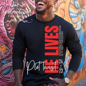 Könnte beinhalten: Schwarzer Pullover mit rotem und weißem Text, der "He Lives" und "Luke 24:23" lautet, mit den Worten "Plot Twist" in weißer Kursivschrift unter dem Text.