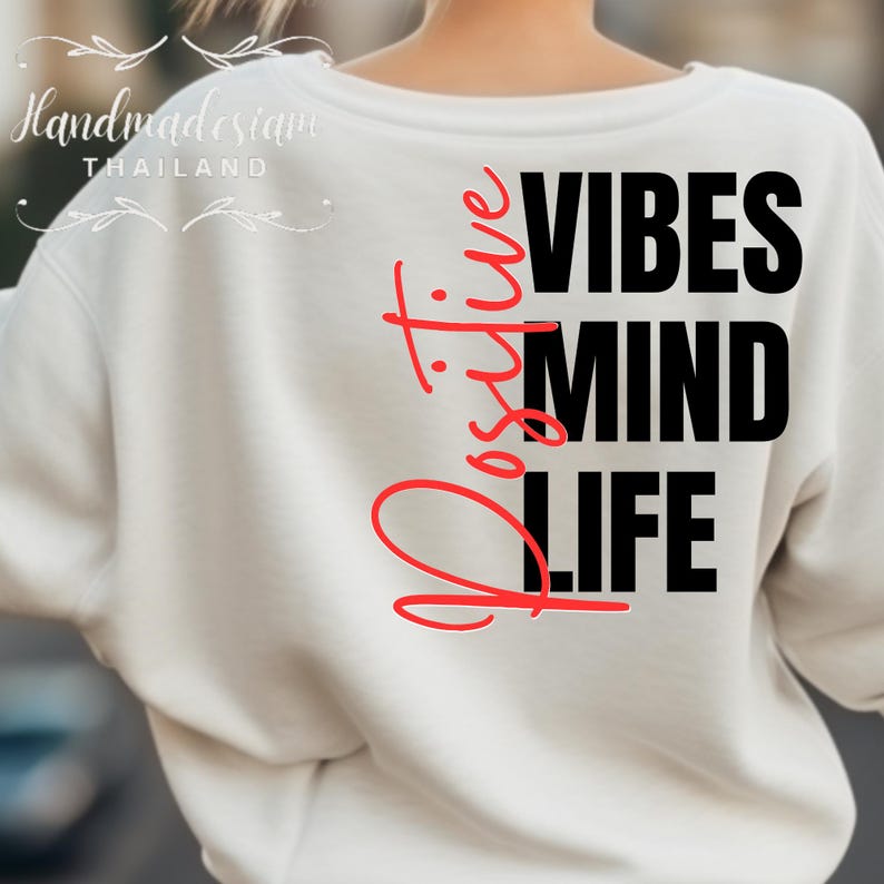 Op de afbeelding: Witte sweatshirt met de woorden "Positive Vibes Mind Life" in zwarte en rode letters. Het woord "Positive" is verticaal in rood geschreven. De sweatshirt heeft een ronde hals.