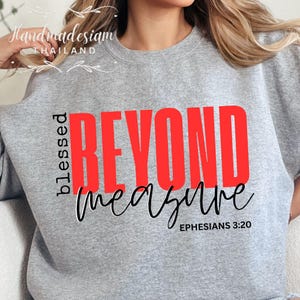 Op de afbeelding: Grijs sweatshirt met de woorden "blessed beyond measure" in rode en zwarte letters. De tekst "Efeziërs 3:20" is in zwart onder de hoofdtekst gedrukt.