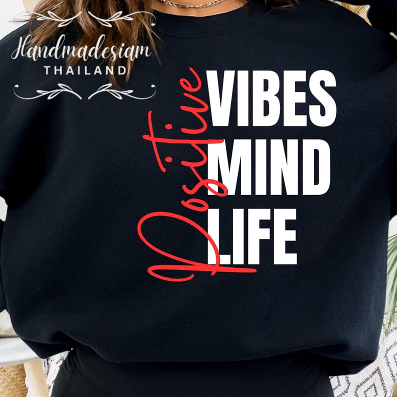 Op de afbeelding: Zwart sweatshirt met de woorden "Positive Vibes Mind Life" in witte en rode letters. De woorden zijn verticaal gestapeld. Het merk "Handmadesiam Thailand" is linksboven in het wit gedrukt.