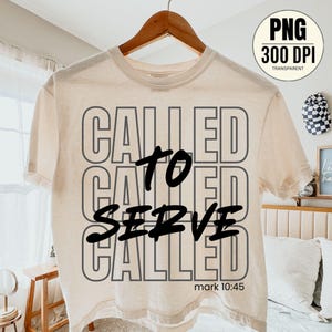 May include: Cream-colored t-shirt with the words "CALLED TO SERVE" in a layered design. The text "mark 10:45" is printed at the bottom. The shirt is hanging on a wooden hanger.