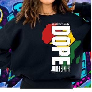 Puede incluir: Sudadera negra con un gráfico blanco de un contorno de África en colores rojo, amarillo y verde. La palabra "DOPE" está escrita verticalmente en letras blancas con el texto "unapologetically" arriba y "JUNETEENTH" abajo.