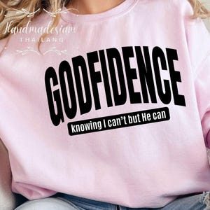 May include: Pink sweatshirt with the text "GODFIDENCE knowing I can't but He can" in black.