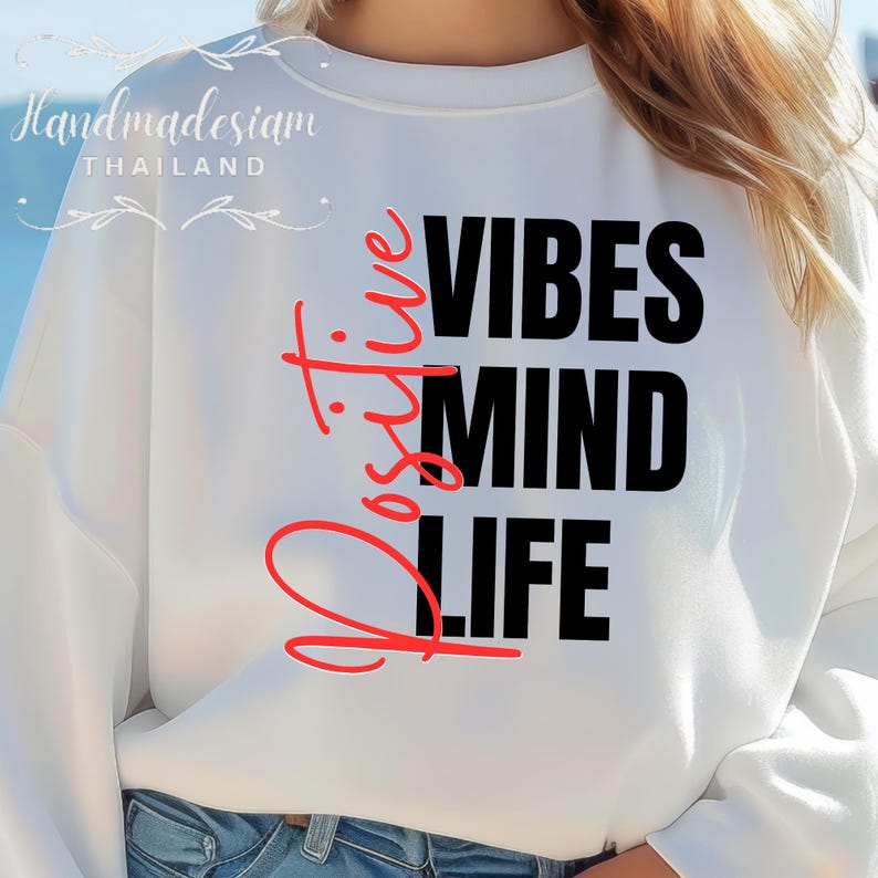 Op de afbeelding: Witte sweatshirt met de woorden "Positive Vibes Mind Life" in zwarte en rode letters. Het woord "Positive" is in cursieve letters. De sweatshirt heeft lange mouwen.