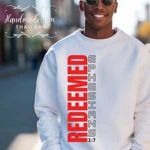 Puede incluir: Sudadera blanca con un gráfico vertical rojo que dice "REDEEMED" y "EPHESIANS 1:7" en texto negro.