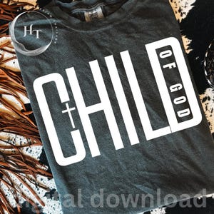 May include: Dark grey t-shirt featuring the words "CHILD OF GOD" in large white block letters. The word "CHILD" has a cross. The shirt is a Comfort Colors brand.
