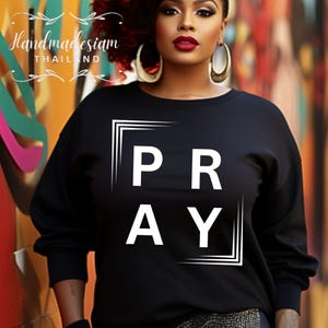 Puede incluir: Sudadera negra con un gráfico blanco que dice "PRAY" en un cuadro.