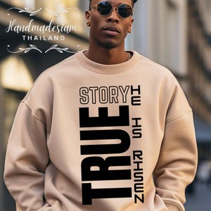May include: A beige sweatshirt with black text that reads "The Story He Is Risen True".