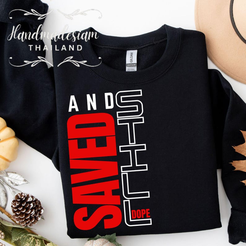 May include: Black sweatshirt with white text that reads "Still Dope" and "Saved" in red. The text is vertically aligned on the left side of the sweatshirt.
