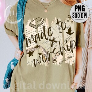 May include: Olive green t-shirt with the words "made to worship" in a distressed font. The design includes a cross, dove, stars, and a book illustration. The text "psalm 95:1" is also visible.