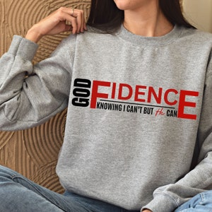 May include: Gray sweatshirt with the text "GOD FIDENCE" in red and black. The text "KNOWING I CAN'T BUT He CAN" is written in black below the main text.