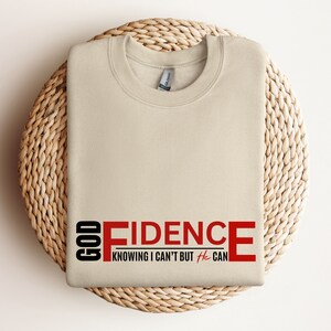 May include: Beige sweatshirt with the text "GOD FIDENCE" in red and black. The text continues with "KNOWING I CAN'T BUT He CAN".