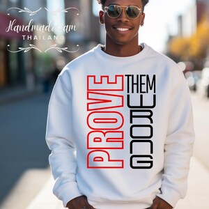 May include: White sweatshirt with the words "PROVE THEM WRONG" printed in red and black letters.