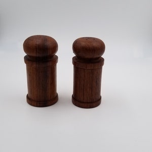 May include: A set of two wooden salt and pepper shakers. The shakers are made of dark brown wood and have a simple, cylindrical design.