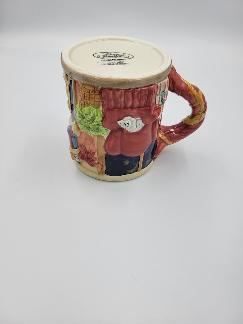 Pode incluir: Uma caneca de cer&acirc;mica com um design detalhado e colorido. A caneca apresenta um casaco vermelho, uma roupa azul e uma al&ccedil;a decorativa. A caneca tem uma borda creme e uma cena detalhada de uma pessoa. A caneca &eacute; um item decorativo.